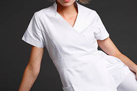 Femme esthéticienne portant une blouse blanche courte à manches claires, pose dynamique sur fond gris. comment choisir blouse esthétique