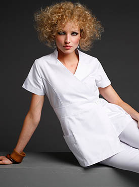Femme esthéticienne portant une blouse blanche courte à manches claires, pose dynamique sur fond gris. comment choisir blouse esthétique